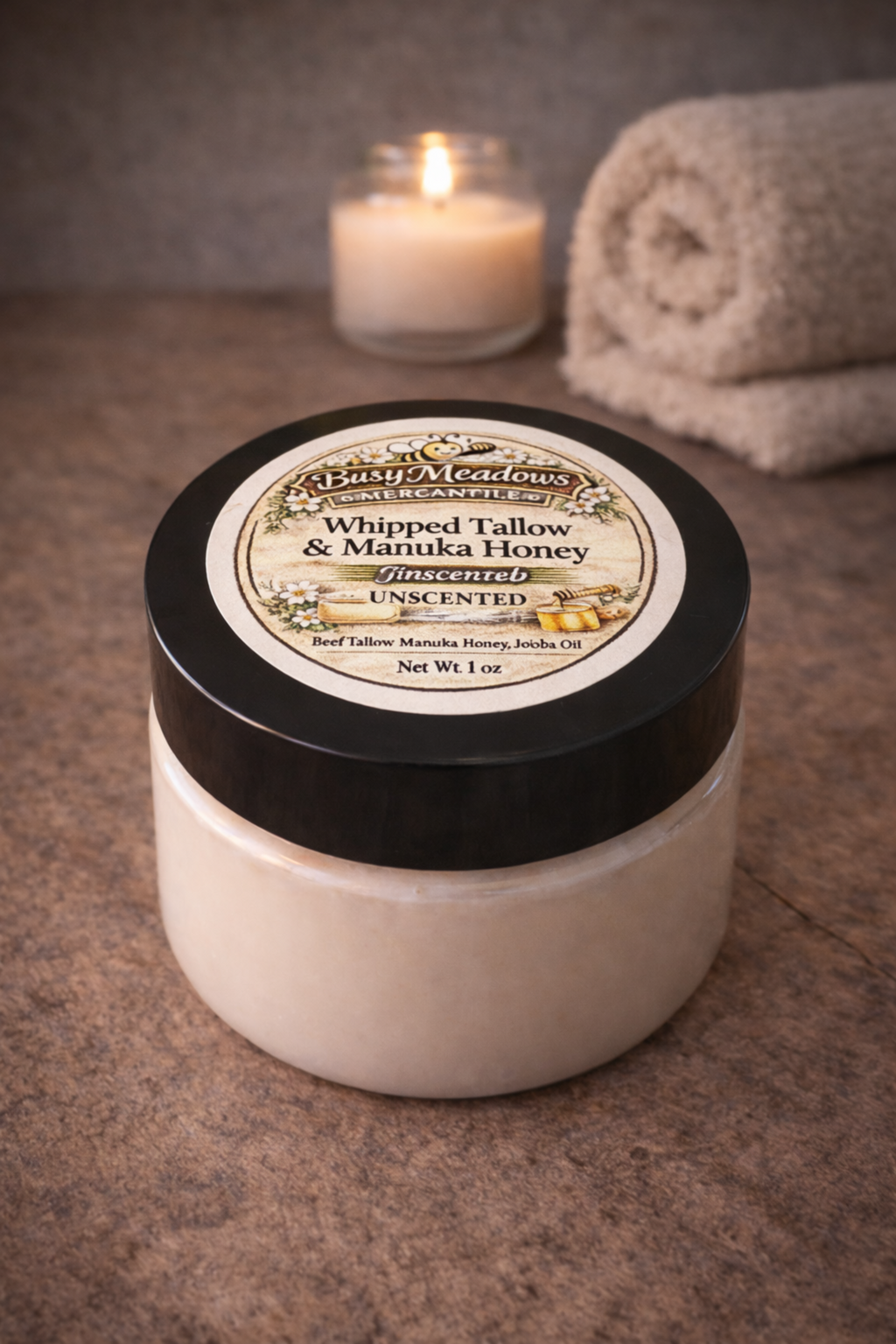 Jar of whipped tallow and manuka honey on a textured surface with a candle and towel in the background.